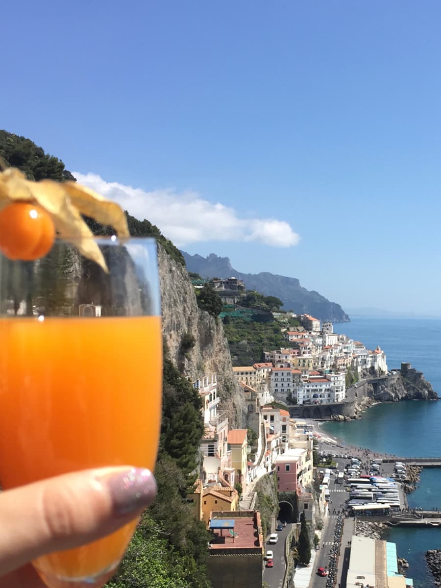 An orange cocktail held up in front of a coastline