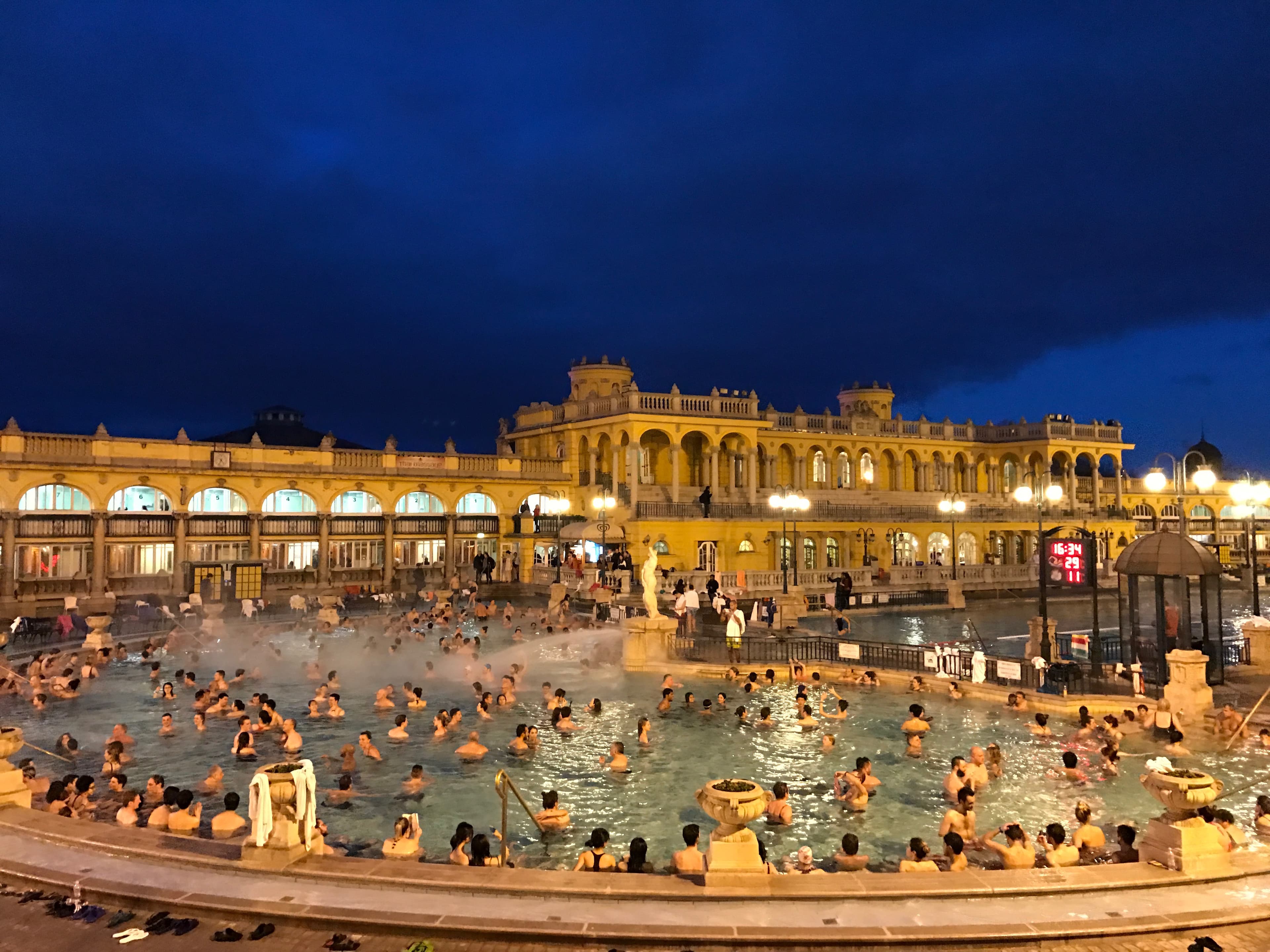 A large fountain with city residents enjoying the outdoor water and night sky