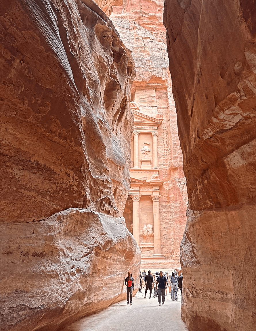 Tourists walking down a path to a temple carved into the stone with large rock walls surrounding them.