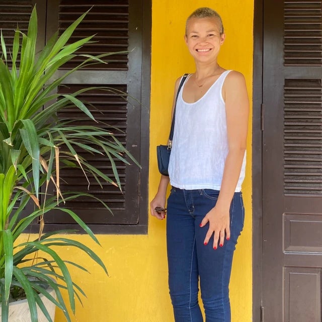 Travel advisor Sequoia Armstrong posing in front of a stone wall and wooden door, while wearing a light blue top.